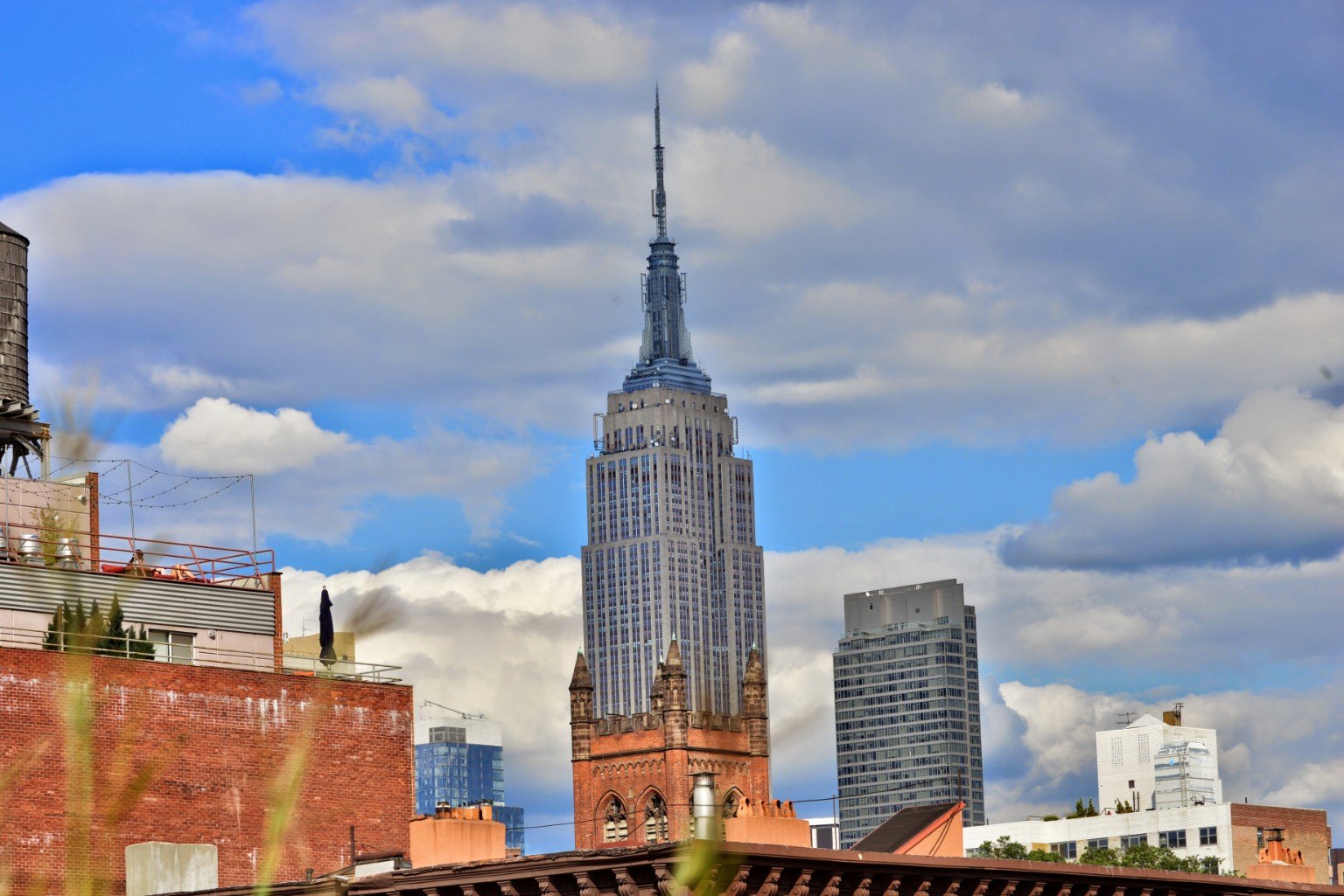 Empire State Building framed by clouds and rooftops